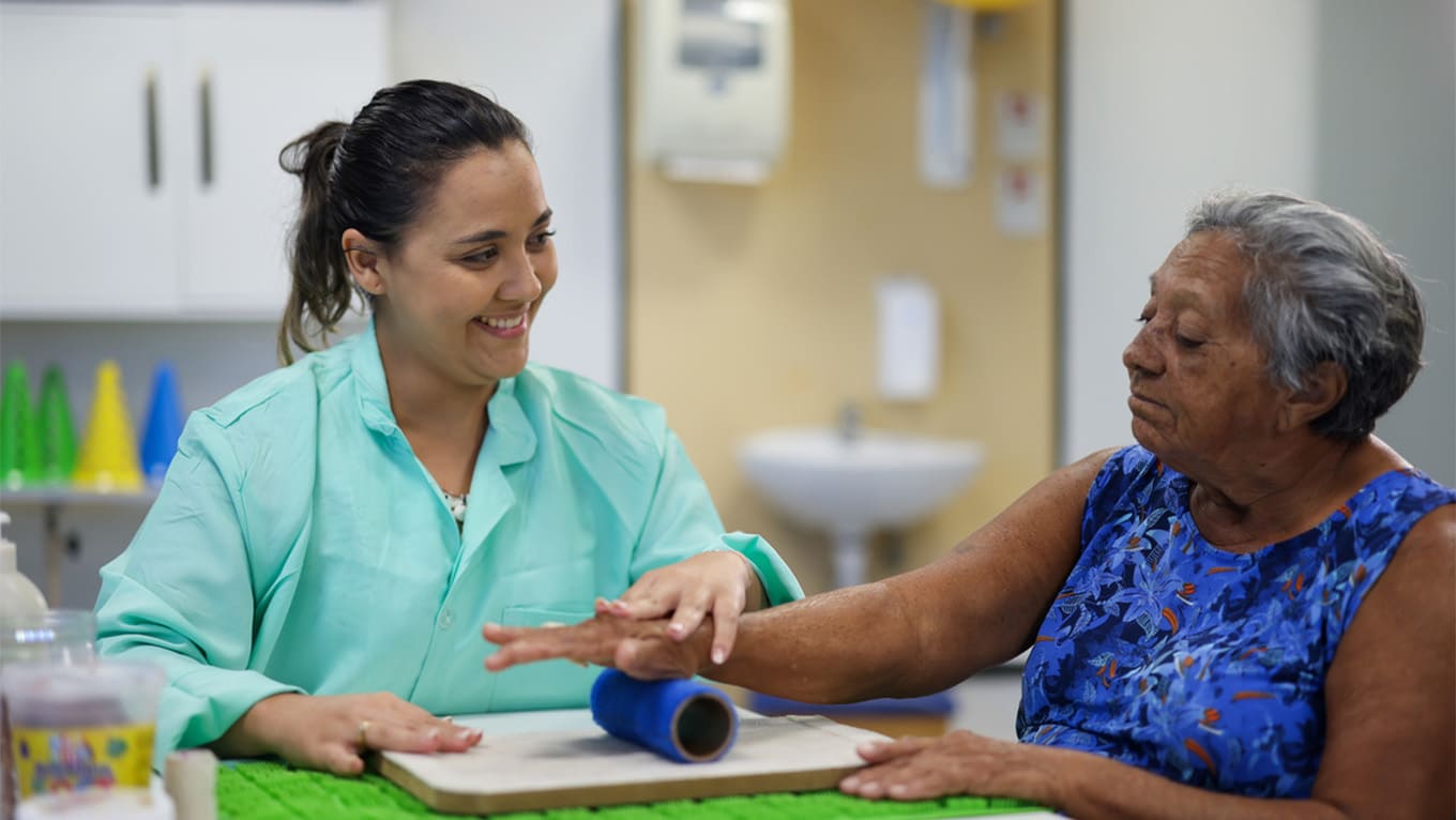 Mão de idoso e de terapeuta em evidência na prática de exercício.