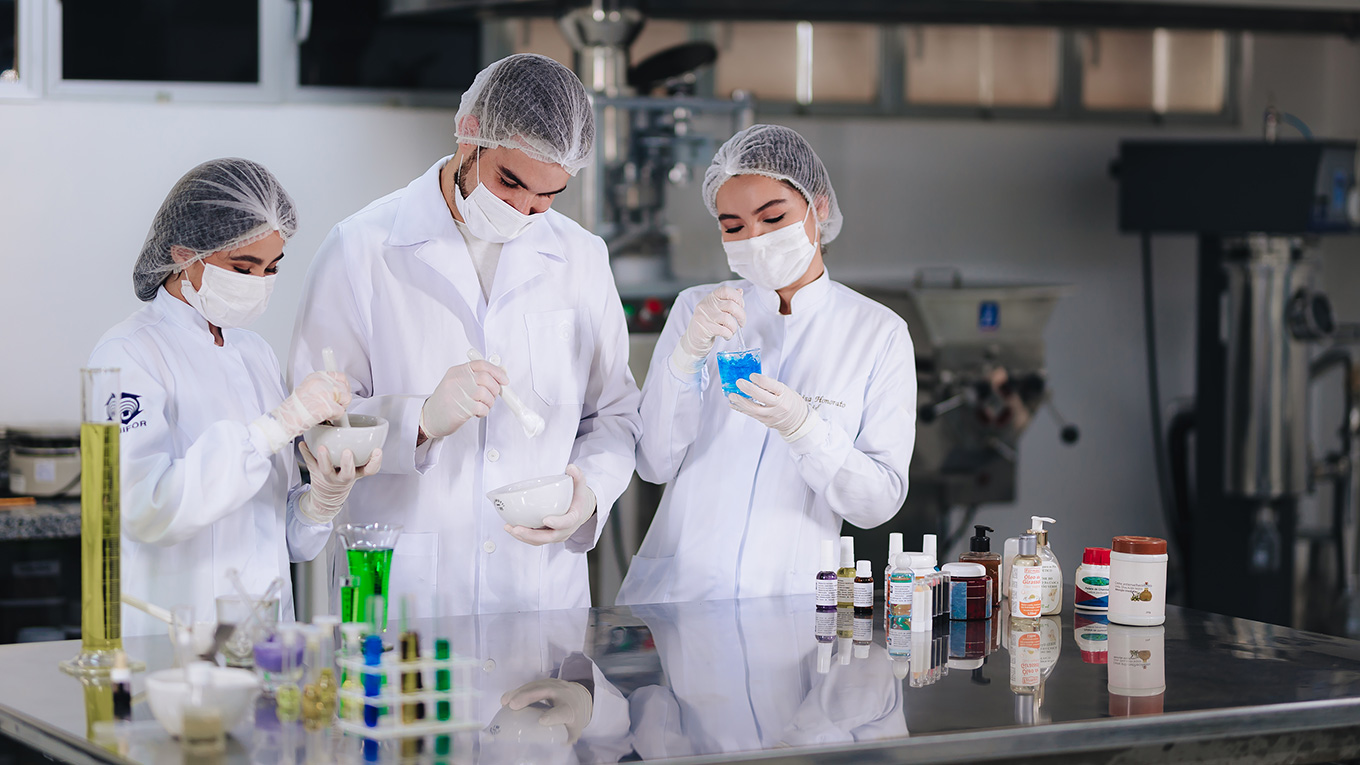 Estudantes com trajes de farmacêutico manipulam tubo de ensaio