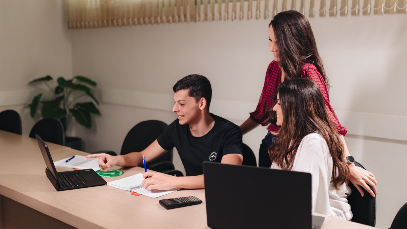 Três jovens interagem e sorriem diante de um notebook