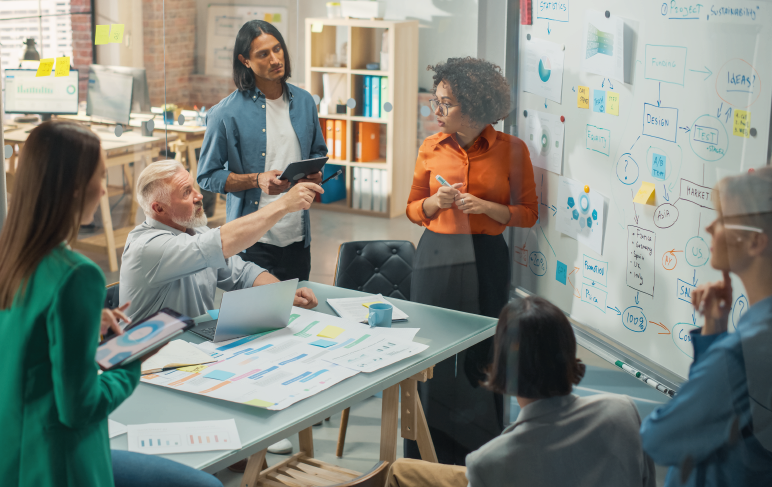 Empresária negra lidera reuniões de negócios com gerentes, conversa e explica estatísticas, usando um quadro branco com gráficos.