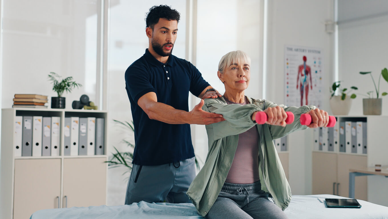 Fisioterapeuta atende paciente que segura pesos com os dois braços à frente do corpo