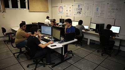 Estudantes realizam pesquisas num laboratório com computadores.