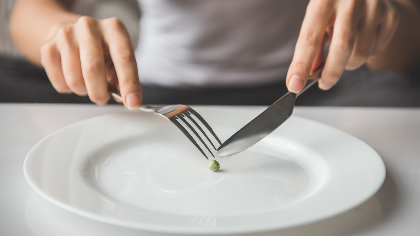 Uma pessoa manipula um grão sobre o prato com garfo e faca.